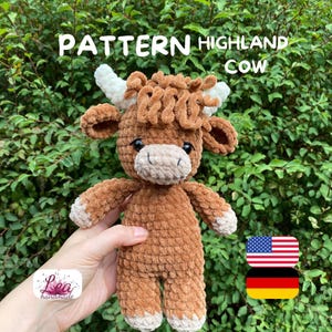 Könnte beinhalten: Ein handgefertigtes gehäkeltes Highland-Kuh-Plüschtier in Braun und Weiß. Das Plüschtier hat weiße Hörner, eine flauschige braune Mähne und eine hellbraune Schnauze. Der Text "PATTERN HIGHLAND COW" steht oben. Die Flaggen der USA und Deutschlands sind unten rechts.