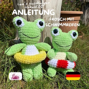 Può includere: Due giocattoli a forma di rana all'uncinetto verde fatti a mano, ciascuno con grandi occhi bianchi e neri e una bocca sorridente. Una rana ha un salvagente giallo e bianco, l'altra un salvagente rosso, bianco e nero. L'immagine include testo in tedesco.