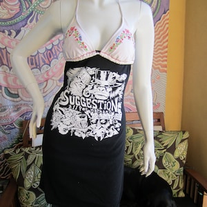 Puede incluir: Un vestido de camiseta negro y blanco con estampado gráfico y un top halter de estampado floral blanco. El vestido presenta un estampado gráfico de un lobo, una calavera y el texto "Suggestion All For Nothing".