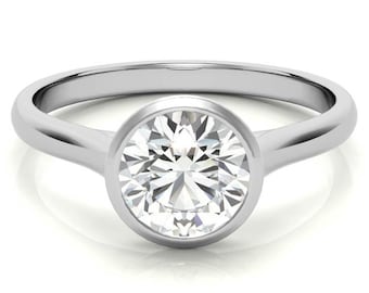 Puede incluir: Un anillo de plata con engaste de bisel que presenta un diamante redondo y transparente.