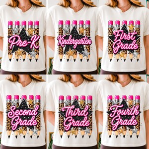 May include: A white t-shirt featuring a graphic of five pencils with leopard print patterns, a large black glittery star, and silver and gold star accents. The text reads Pre-K, Kindergarten, First Grade, Second Grade, Third Grade, or Fourth Grade.