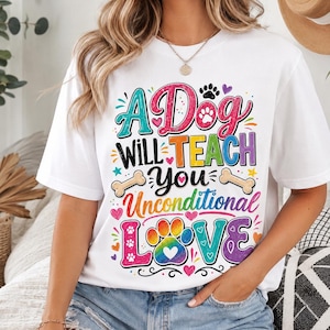 May include: A white short-sleeved t-shirt featuring a colorful graphic with the text A Dog WILL TEACH YOU Unconditional LOVE. The design includes paw prints, hearts, stars, and bone shapes in vibrant shades of pink, blue, yellow, and purple.