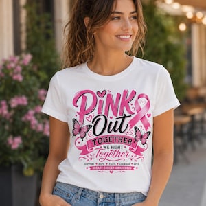 May include: White t-shirt with a pink design that reads "Pink Out Together" with a pink ribbon and butterflies. The shirt also includes the text "We Fight Together" and the words "Support, Hope, Faith, Courage, Love, Breast Cancer Awareness."