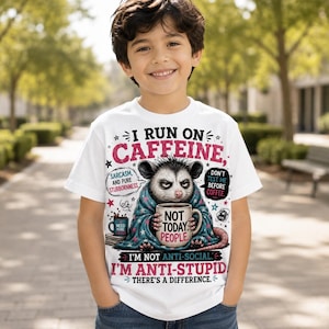 K&ouml;nnte beinhalten: Ein wei&szlig;es T-Shirt mit einer Grafik eines Opossums, das in eine blaue Decke eingewickelt ist und eine Tasse mit der Aufschrift NOT TODAY PEOPLE h&auml;lt. Der Text lautet I RUN ON CAFFEINE, SARCASM AND PURE STUBBORNESS, DON'T TEST ME BEFORE COFFEE, I'M NOT ANTI-SOCIAL. I'M ANTI-STUPID.