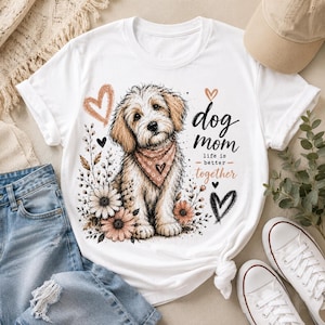 May include: White t-shirt featuring a cute dog illustration with a pink bandana, surrounded by flowers and hearts. The text "dog mom life is better together" is printed on the shirt. A casual, everyday wear tee.