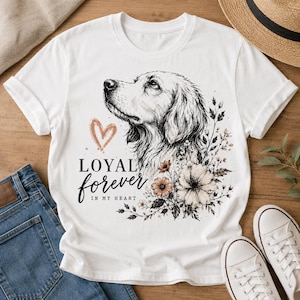 May include: White t-shirt featuring a detailed illustration of a dog's face, accompanied by floral accents and the words "LOYAL forever IN MY HEART" in a script font. The shirt is paired with blue jeans and white sneakers.