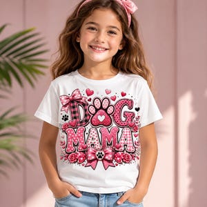 May include: White t-shirt with a pink and black "Dog Mama" graphic. The design includes a paw print, hearts, bows, and roses. The shirt is decorated with a plaid pattern and a heart-shaped paw print.