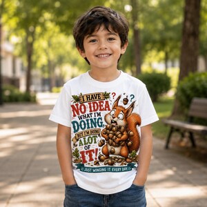 K&ouml;nnte beinhalten: Ein wei&szlig;es Kurzarm-T-Shirt mit einer Grafik eines braunen Eichh&ouml;rnchens, das viele Eicheln h&auml;lt. Der Text lautet: I HAVE NO IDEA WHAT I'M DOING, BUT I'M DOING A LOT OF IT! JUST WINGING IT EVERY DAY. Das Design enth&auml;lt bunte Schriftz&uuml;ge und Eichenbl&auml;tter.