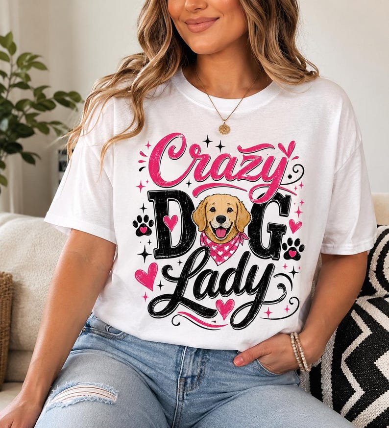 May include: A white short-sleeved t-shirt featuring a graphic print with the text "Crazy Dog Lady" in black and pink lettering. The design includes a golden retriever illustration wearing a pink bandana, surrounded by pink hearts and black paw prints.