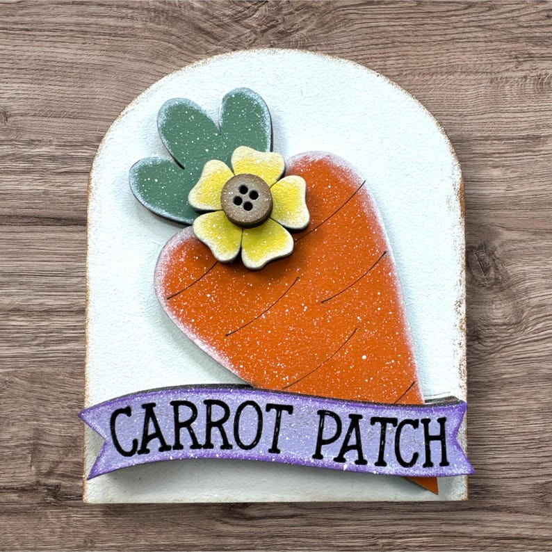 Pode incluir: Decora&ccedil;&atilde;o de P&aacute;scoa em madeira com uma grande cenoura laranja, folhas verdes e uma flor amarela com um bot&atilde;o castanho no centro. As palavras "CARROT PATCH" est&atilde;o numa faixa roxa. O fundo &eacute; branco com um tom azul claro.