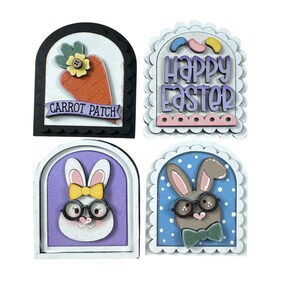 Pode incluir: Quatro decora&ccedil;&otilde;es de P&aacute;scoa em madeira. Uma apresenta uma cenoura com o texto "CARROT PATCH". Outra diz "Happy Easter". As outras duas t&ecirc;m rostos de coelho usando &oacute;culos e gravatas borboleta. Todas est&atilde;o em molduras arqueadas.