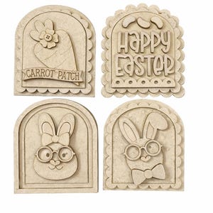 Pode incluir: Quatro decora&ccedil;&otilde;es de P&aacute;scoa em madeira. Uma apresenta uma cenoura com uma flor e o texto "CARROT PATCH". Outra diz "HAPPY EASTER". As outras duas retratam coelhos usando &oacute;culos e gravatas borboleta. Todos s&atilde;o de cor castanho claro.