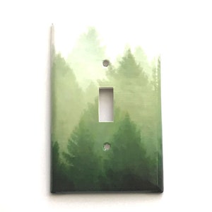 May include: A light switch cover with a watercolor painting of a forest scene. The painting features green and white tones, depicting a misty forest with tall trees.