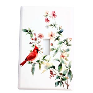 May include: A white light switch cover with a watercolor design of a red cardinal perched on a branch with pink and white flowers.