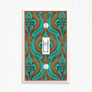 May include: A decorative light switch cover with a brown and teal damask pattern. The switch plate has a white border and a white toggle switch. The design features a repeating floral motif.