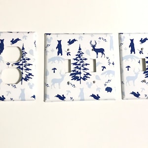 May include: Set of three light switch covers with a white background and a repeating pattern of blue forest animals and trees. The covers include a single outlet, a double switch, and a single switch.