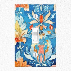 May include: A decorative light switch cover featuring a watercolor floral design. The cover has a vibrant blue background with orange, yellow, and pink floral elements. The switch is white.