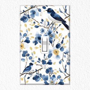 May include: White light switch cover featuring a watercolor design of blue birds, flowers, and gold accents. The floral pattern includes blue blossoms and gold leaf details, creating a nature-inspired aesthetic. The switch is a standard toggle style.