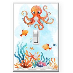 May include: A light switch cover featuring an orange octopus with blue eyes swimming above a coral reef with orange and yellow fish. The background is a light blue watercolor wash.