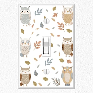 May include: White light switch cover decorated with six cartoon owls in various colors, including gray, brown, and beige. The cover also features leaf and berry accents in muted tones.