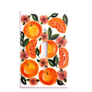 May include: A white light switch cover with a painted design of oranges and pink flowers. The oranges are sliced and whole, and the flowers are stylized.