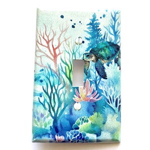 May include: A light blue, green, and pink watercolor light switch cover with a sea turtle swimming through coral reefs.