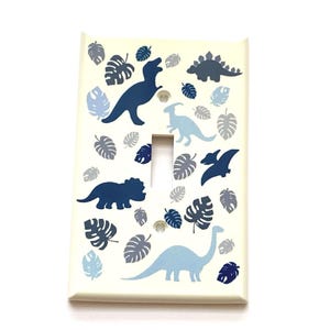 May include: A white light switch cover with a blue and gray dinosaur and leaf pattern.