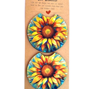 May include: Two round car coasters with a sunflower design. The coasters are printed with a vibrant sunflower with yellow petals and a dark brown center. The background of the coasters is a blue and green watercolor design. The text on the card reads "Car Coaster" and "Life can get messy, but your car doesn't have to. Our car coasters help keep your cup holders clean."