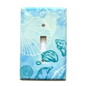 May include: Light blue light switch cover with a watercolor background and a pattern of seashells in teal.