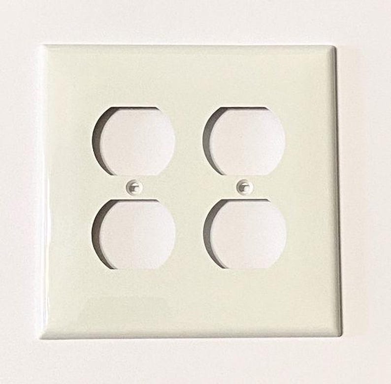 May include: White plastic electrical outlet cover with two double outlets.
