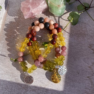 May include: A set of four beaded bracelets with charms. The bracelets are made with yellow, green, pink, red, and black beads. The charms are silver and gold with star designs.