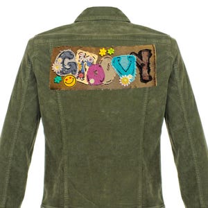 May include: Olive green jacket with a patch on the back that reads "Groovy" in colorful, embroidered letters. The letters are decorated with flowers and a smiley face. The jacket has a button-down front and a collar.