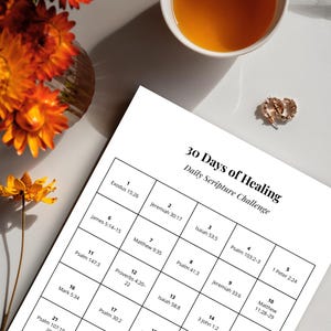 May include: A white paper with a grid layout titled "30 Days of Healing Daily Scripture Challenge" sits on a white surface. A cup of tea, a vase of orange flowers, and gold earrings are also present.