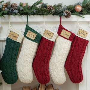 Peut inclure: Cinq chaussettes de Noël en tricot avec des étiquettes en bois personnalisées. Les chaussettes sont en vert, blanc et rouge.