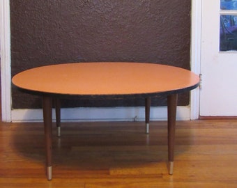 May include: A light pink oval-shaped table with a dark wood base and silver legs. The table is sitting on a wooden floor.