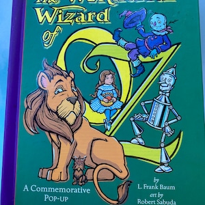 May include: A green pop-up book titled "The Wonderful Wizard of Oz" by L. Frank Baum with art by Robert Sabuda. The cover features illustrations of Dorothy, the Cowardly Lion, the Tin Man, and the Scarecrow.