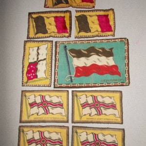 May include: A collection of vintage fabric flag patches. The flags include the colors of black, yellow, and red, with the word "BELGIUM" on some. Other flags feature the colors of black, white, and red, with the word "GERMANY".