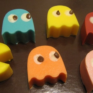 May include: Five colorful Pac-Man shaped candies with chocolate eyes. The candies are yellow, blue, orange, pink, and red.