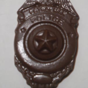 May include: A brown chocolate police badge with a five-pointed star in the center and the words "Police" and "Law Enforcement" around the star.