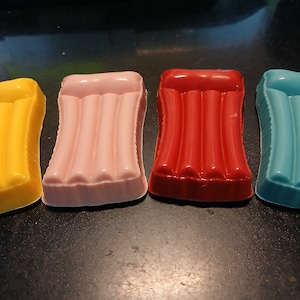 May include: Four inflatable pool float toys made of chocolate. The floats are yellow, pink, red, and blue. Each float has three air chambers.