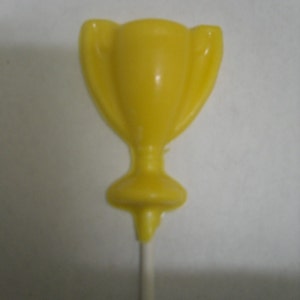May include: A yellow chocolate trophy on a stick. The trophy is shaped like a traditional cup with two handles.