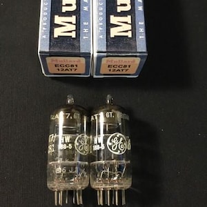 May include: Two clear glass vacuum tubes with the text "GE" and "12AT7" printed on them, alongside two boxes labelled "Mullard ECC81 12AT7". The boxes are blue and white.