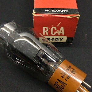 May include: An RCA Radiotron 5R4GY electron tube with a clear glass bulb and a brown base featuring metal pins. The tube is accompanied by its original red and white cardboard box, which displays the RCA logo and the text Electron Tube.