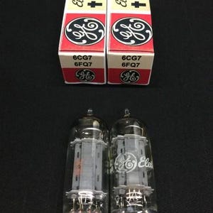May include: Two electronic vacuum tubes with clear glass and metal pins, next to their original boxes. The boxes are white with red accents, featuring the text "Electronic tube" and the GE logo. The tube model numbers are 6CG7 and 6FQ7.