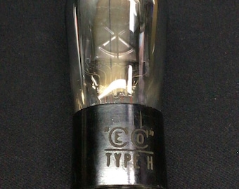 Może przedstawiać: Przezroczysta szklana lampa próżniowa z czarną podstawą, na której nadrukowano biały napis "CO" oraz "TYPE H". Lampa posiada cztery metalowe piny wystające z dołu oraz wewnętrzne druciane żarniki widoczne przez przezroczystą szklaną bańkę.