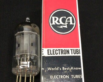 May include: A clear glass vacuum tube with internal metal components and a base with multiple pins, positioned next to a rectangular cardboard box labeled RADIOTRON RCA ELECTRON TUBI and World's Best-Known ELECTRON TUBES in red, white, and black.