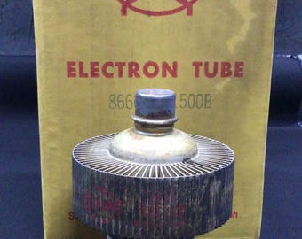 Może przedstawiać: Zabytkowa lampa elektronowa Eimac z cylindryczną ceramiczną podstawą i dużym metalowym radiatorem, umieszczona przed oryginalnym żółtym kartonowym pudełkiem z czerwonym logo Eimac i napisem Electron Tube 866 1500B.