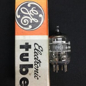 Peut inclure: Une boîte orange et blanche avec le logo GE et les mots "Electronic tube" à côté d'un tube électronique en verre transparent avec des broches métalliques. Le tube porte le logo GE et d'autres textes.