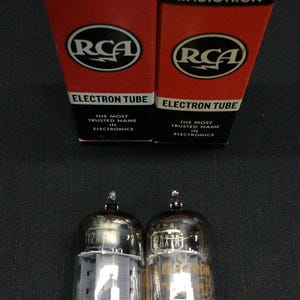 May include: Two RCA Radiotron 12AX7A/ECC83 valve tubes with their original red and black boxes. The boxes feature the RCA logo and the text "Electron Tube". The tubes are glass with metal bases.