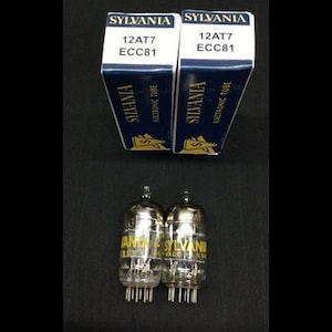 Puede incluir: Dos válvulas de vacío electrónicas Sylvania 12AT7 ECC81 con sus cajas originales. Las cajas son blancas y azul marino con el logotipo de Sylvania y las especificaciones del tubo. Los tubos son de vidrio transparente con letras amarillas.